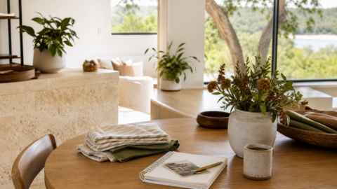 Quiet home table with folded linens, notebook, coffee, flowers, and soft natural light.