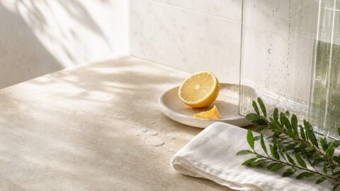 Lemon, natural linen, greenery, water droplets, stone tile, and clear glass in soft window light.