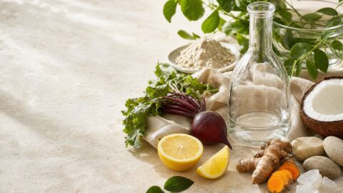 Citrus, coconut, beet, turmeric, minerals, botanicals, and a clear refillable vessel on pale travertine.