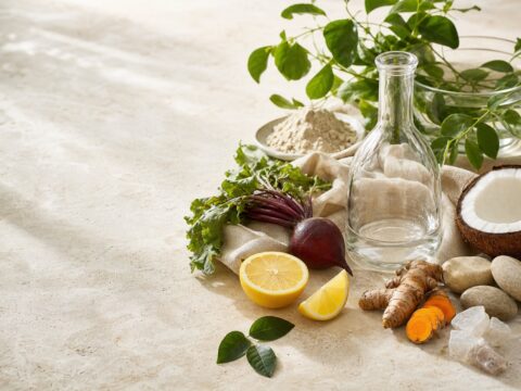 Citrus, coconut, beet, turmeric, minerals, botanicals, and a clear refillable vessel on pale travertine.