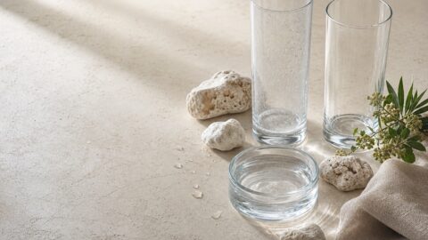 Two clear glasses show the contrast between subtle hard-water spotting and clean glass beside water and mineral stones.