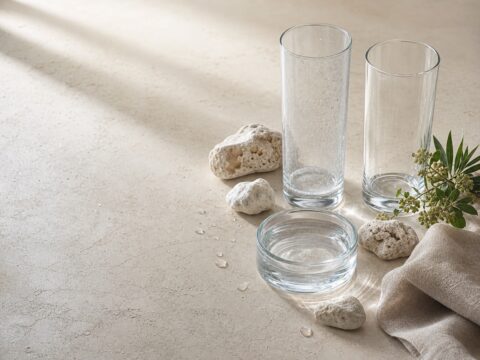 Two clear glasses show the contrast between subtle hard-water spotting and clean glass beside water and mineral stones.