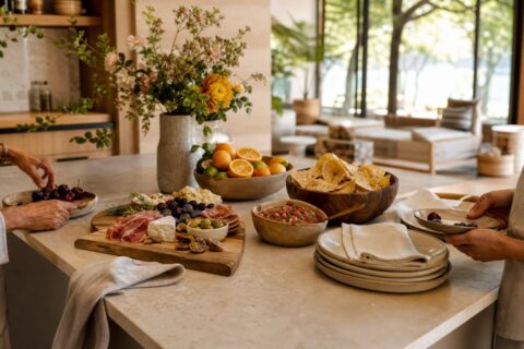 Relaxed kitchen island with charcuterie, fruit, chips and salsa, flowers, linen napkins, and warm natural light.