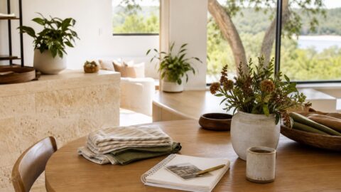 Quiet home table with folded linens, notebook, coffee, flowers, and soft natural light.