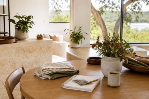 Quiet home table with folded linens, notebook, coffee, flowers, and soft natural light.