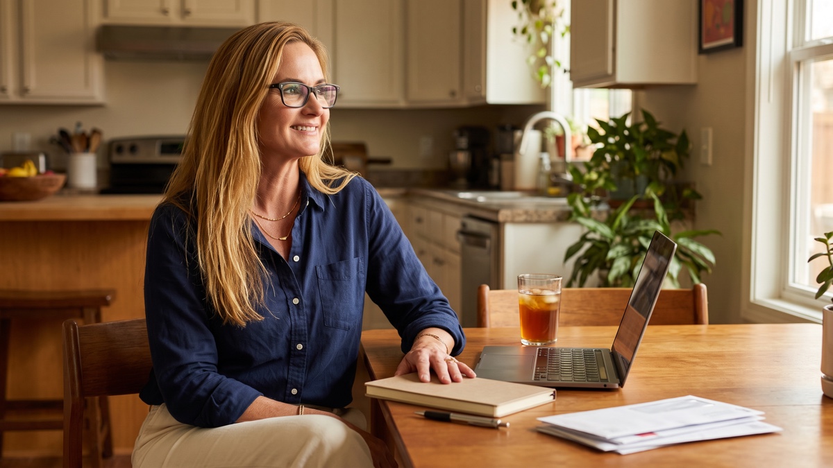 Jennifer pauses thoughtfully at a home worktable in soft morning light.